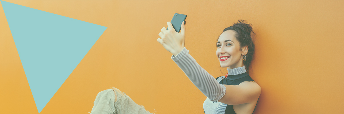 Eine Social-Media Influencerin lehnt sich an eine Wand an und macht mit ihrem Handy ein Selfie